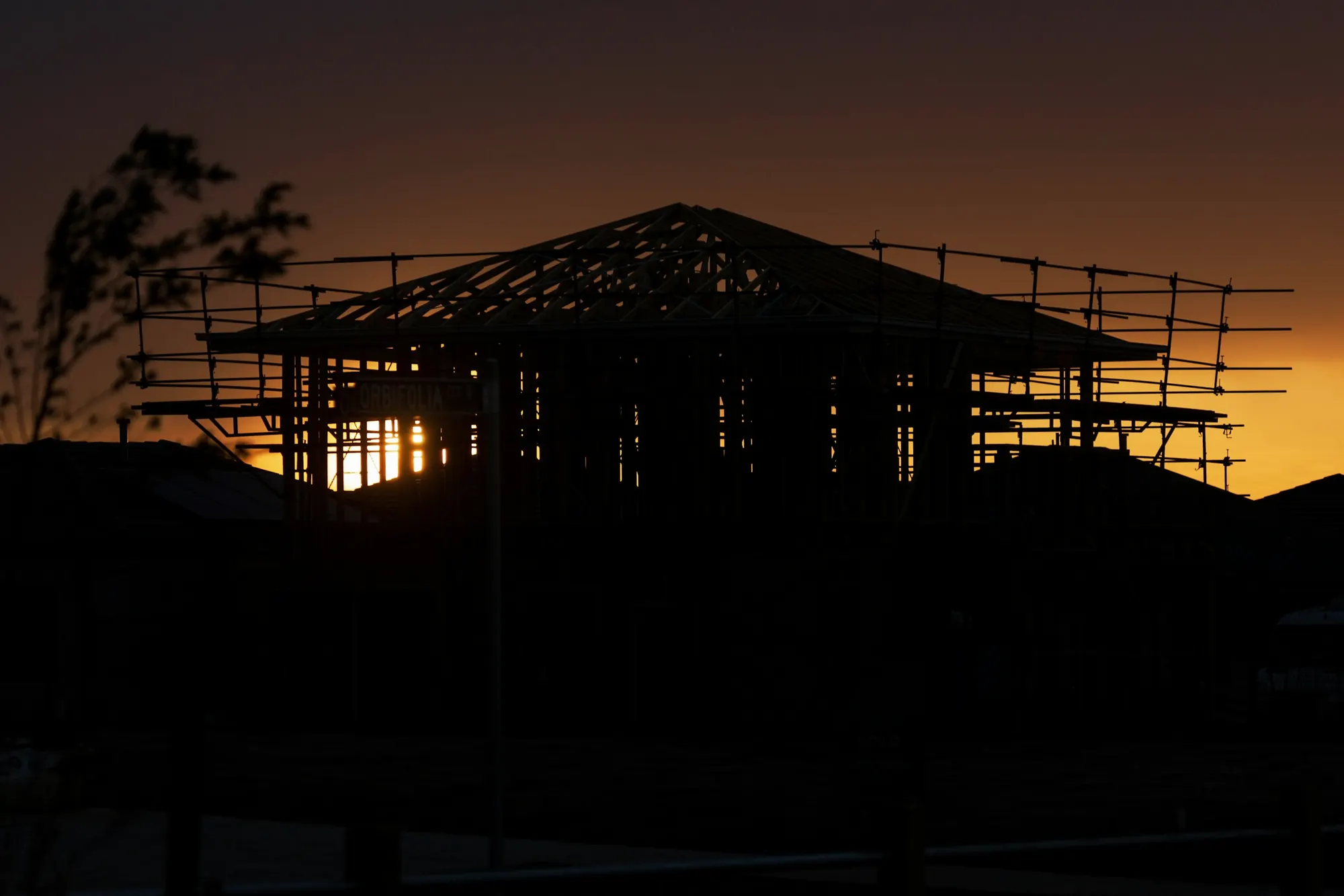 The timber frame of a new house in silhouette against an orange sunrise on a building site