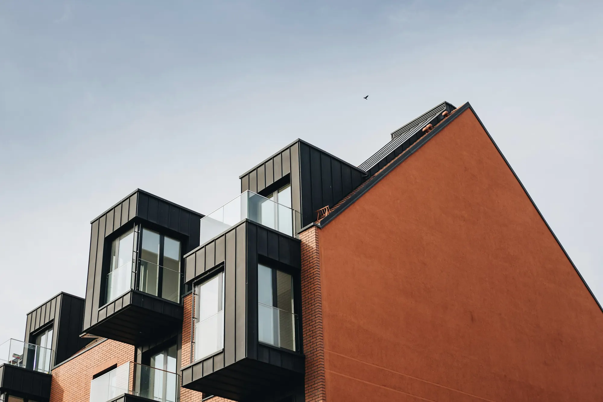 Modern townhouse facade in red brick with dark metal-clad bay windows and glass balconies