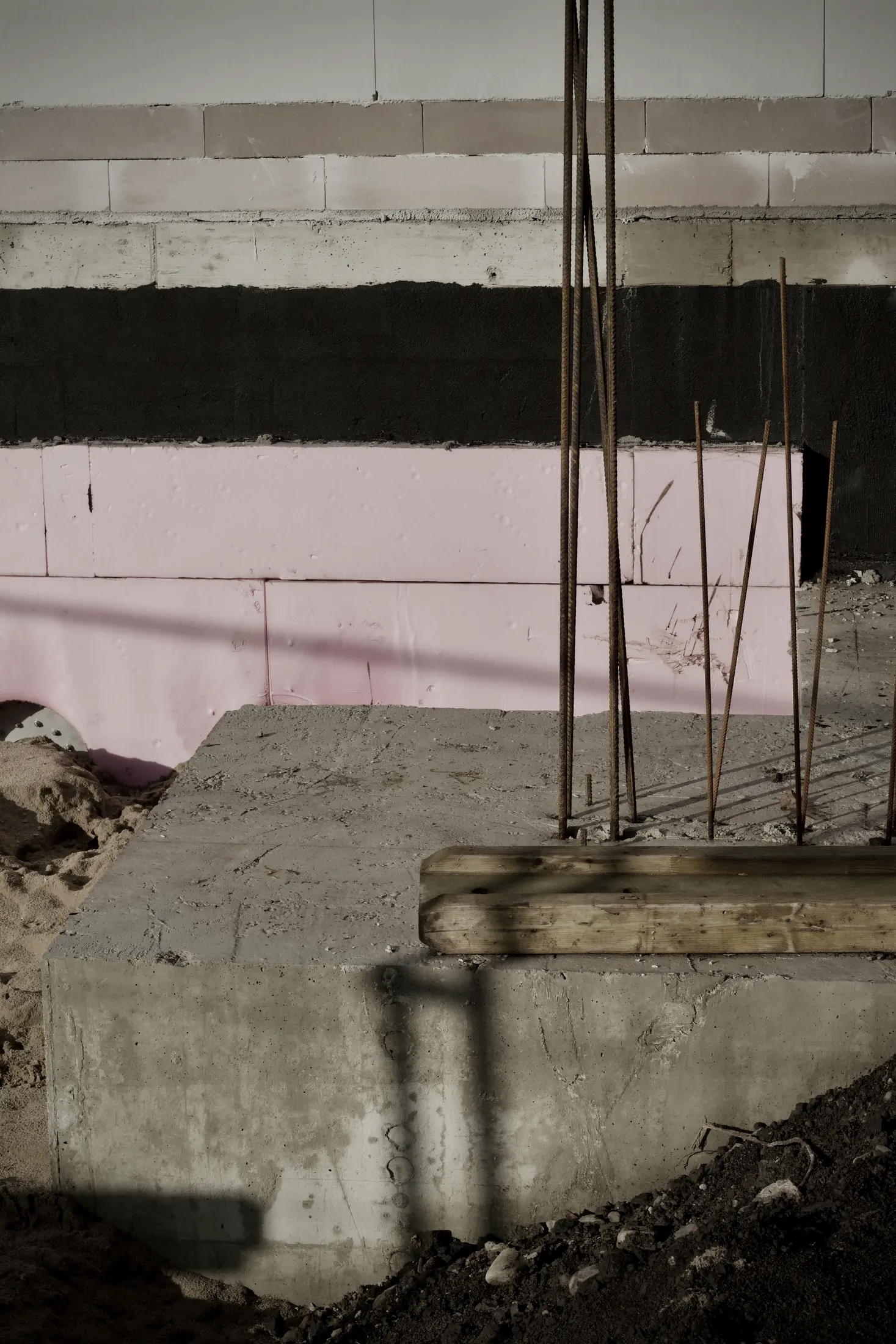 Steel rebar rising from a poured concrete footing beside foam insulation on a residential foundation