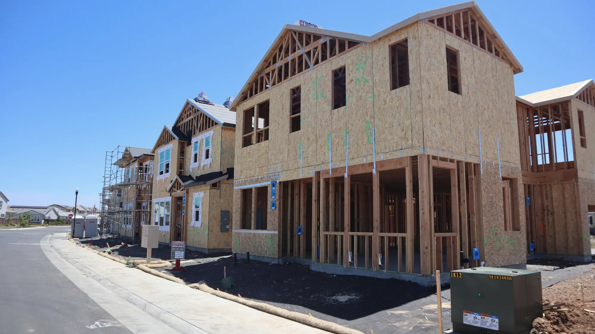Timber-framed three-storey townhomes with gabled roofs under construction, OSB sheathing on the walls